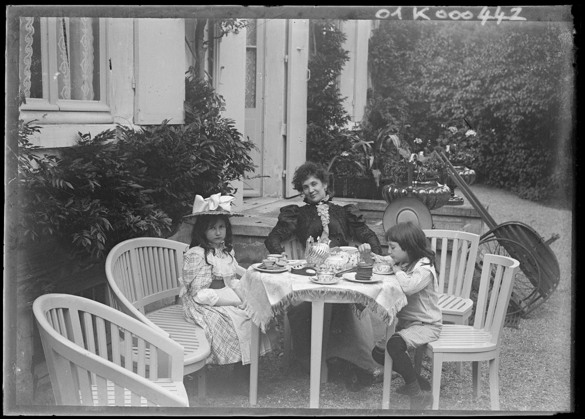 Jeanne Rozerot et les enfants, assis autour de la table du goûter, près du perron de la maison de Verneuil, une photo d’Émile Zola